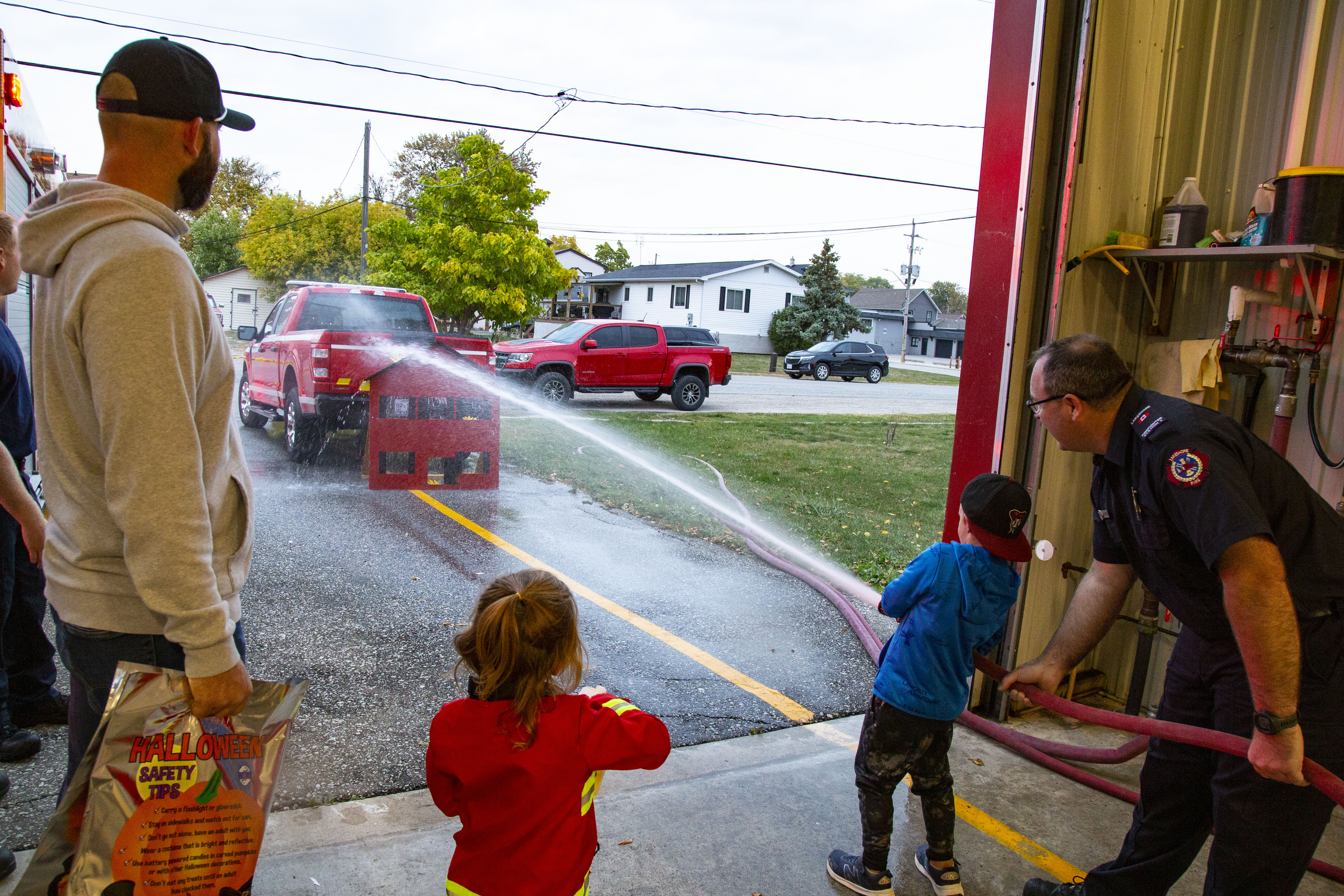 Image of a child with firefighter spraying a fire hose. 