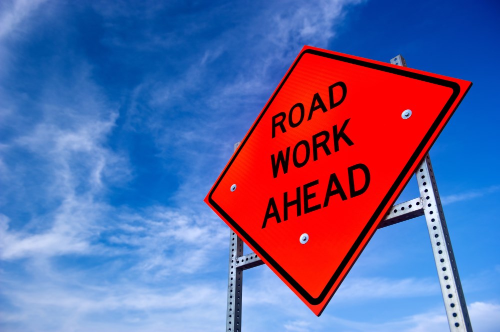 Image of a "road work ahead" sign with the sky as background.