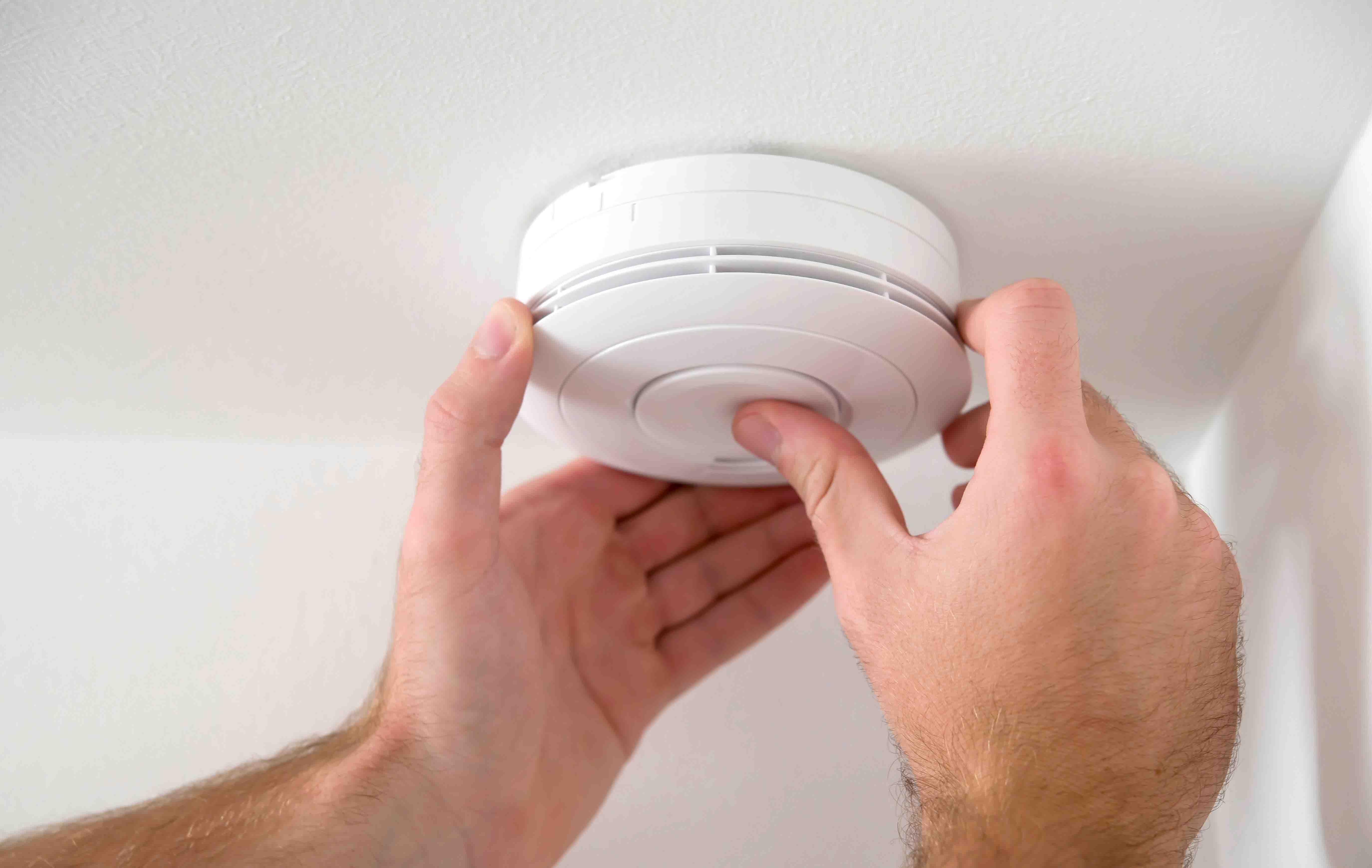 Picture of person checking smoke/CO alarm on ceiling.