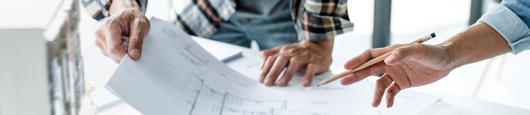 Photo of hands holding pencil while discussing a building plan.