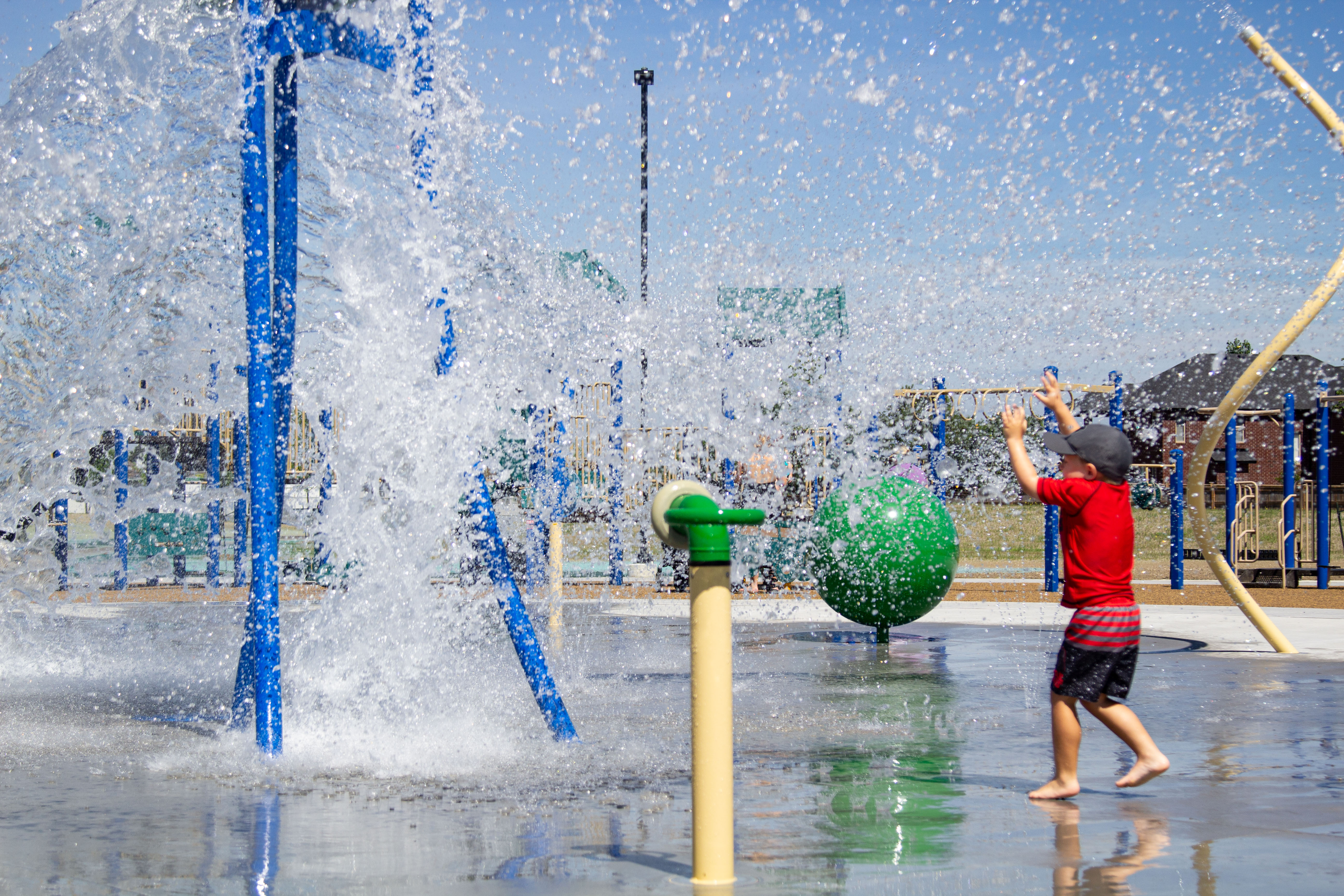 Child holding arms up to a splash pad feature about to spill water at River Ridge Park in Lakeshore