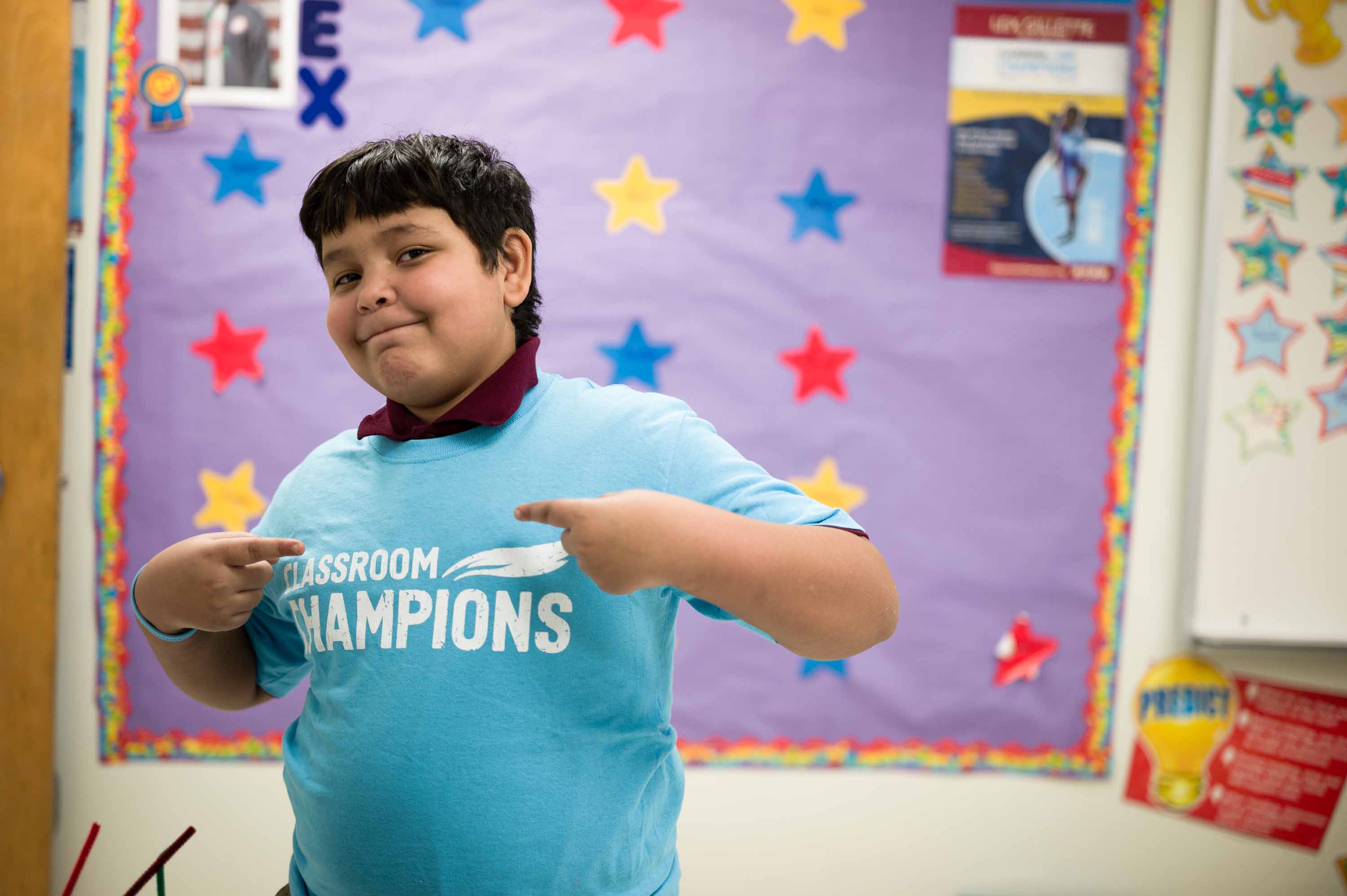 Image of child pointing to their t-shirt which reads "Classroom Champions."