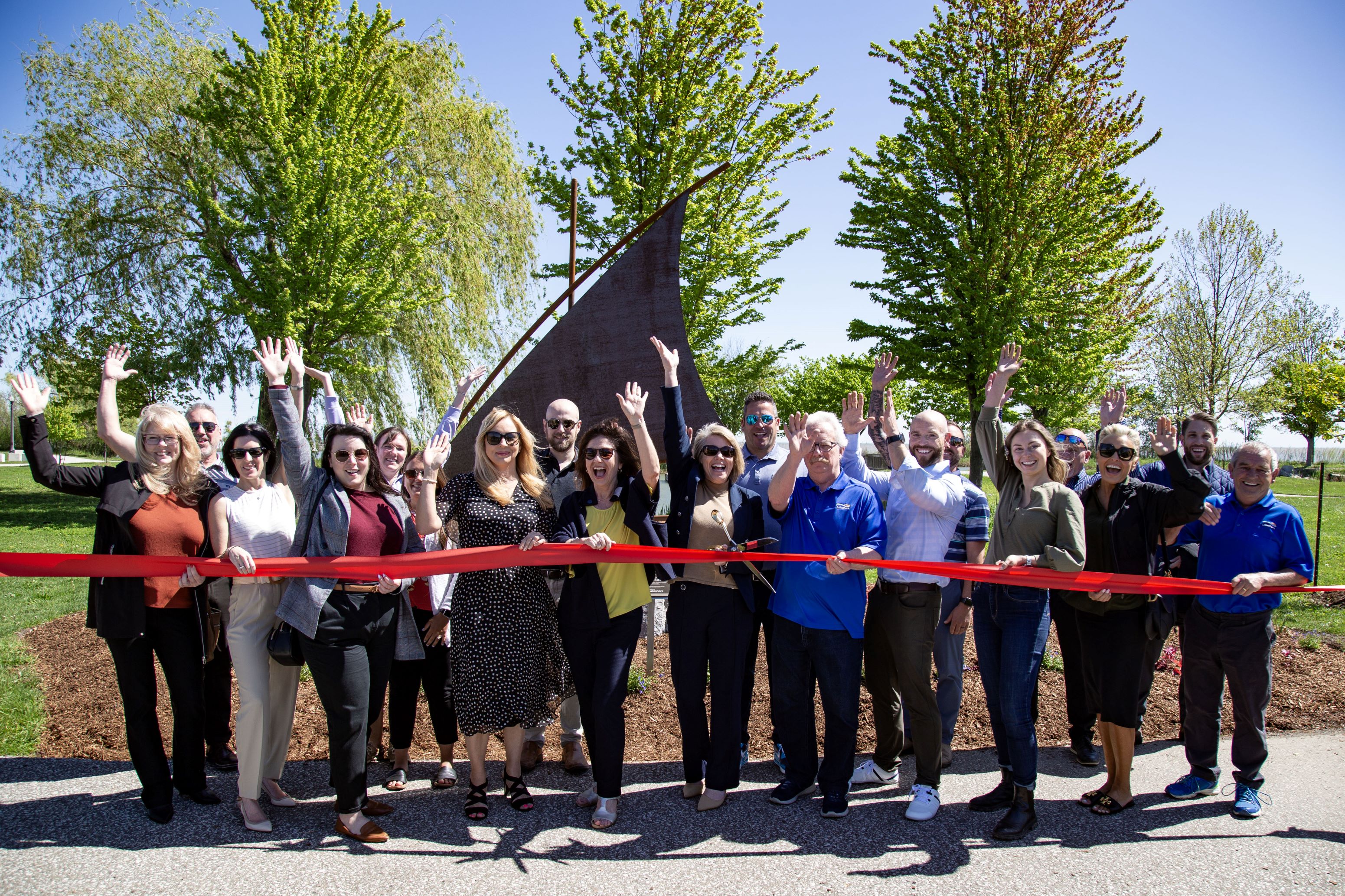 Image of group ribbon cutting in front of sailboat statue at park.
