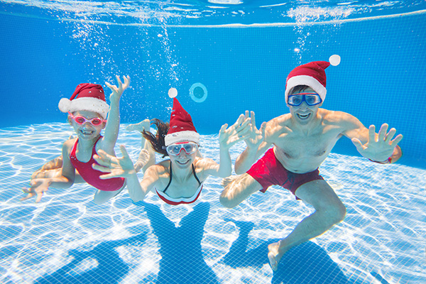 Family swimming underwater while wearing Santa hats