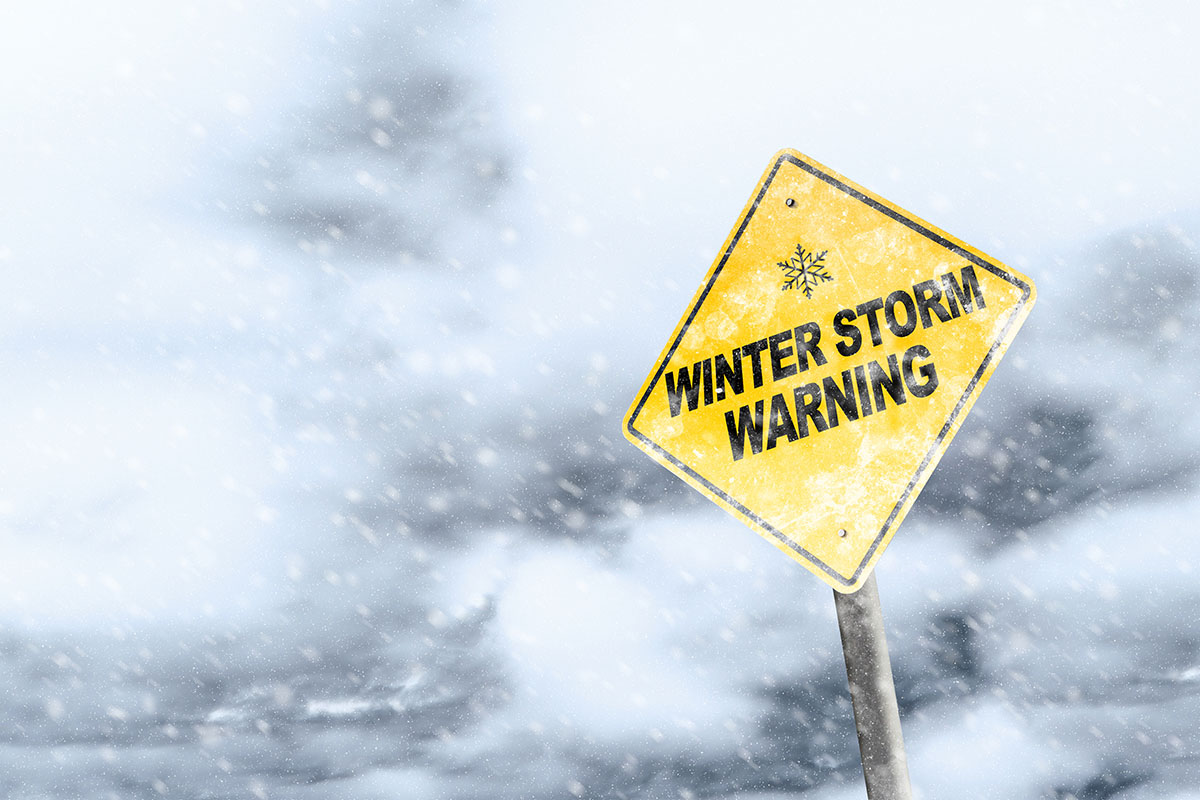 A yellow "winter storm warning" sign shown in blowing snow.