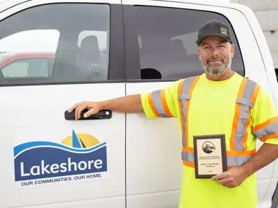 Ron Duquette holding his Truck Roadeo plaque while leaning on a Lakeshore truck.