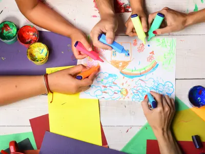 Overhead image of kids with markers colouring on a page.