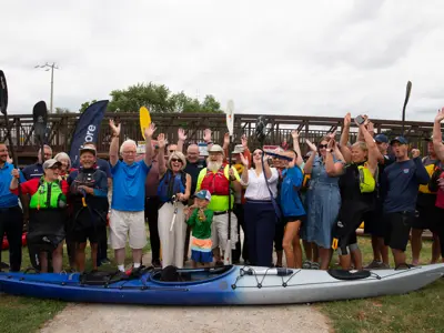 Group photo of council and community members with Kayak in front. Everyone is celebrating the opening of the new accessible kayak and canoe launch.