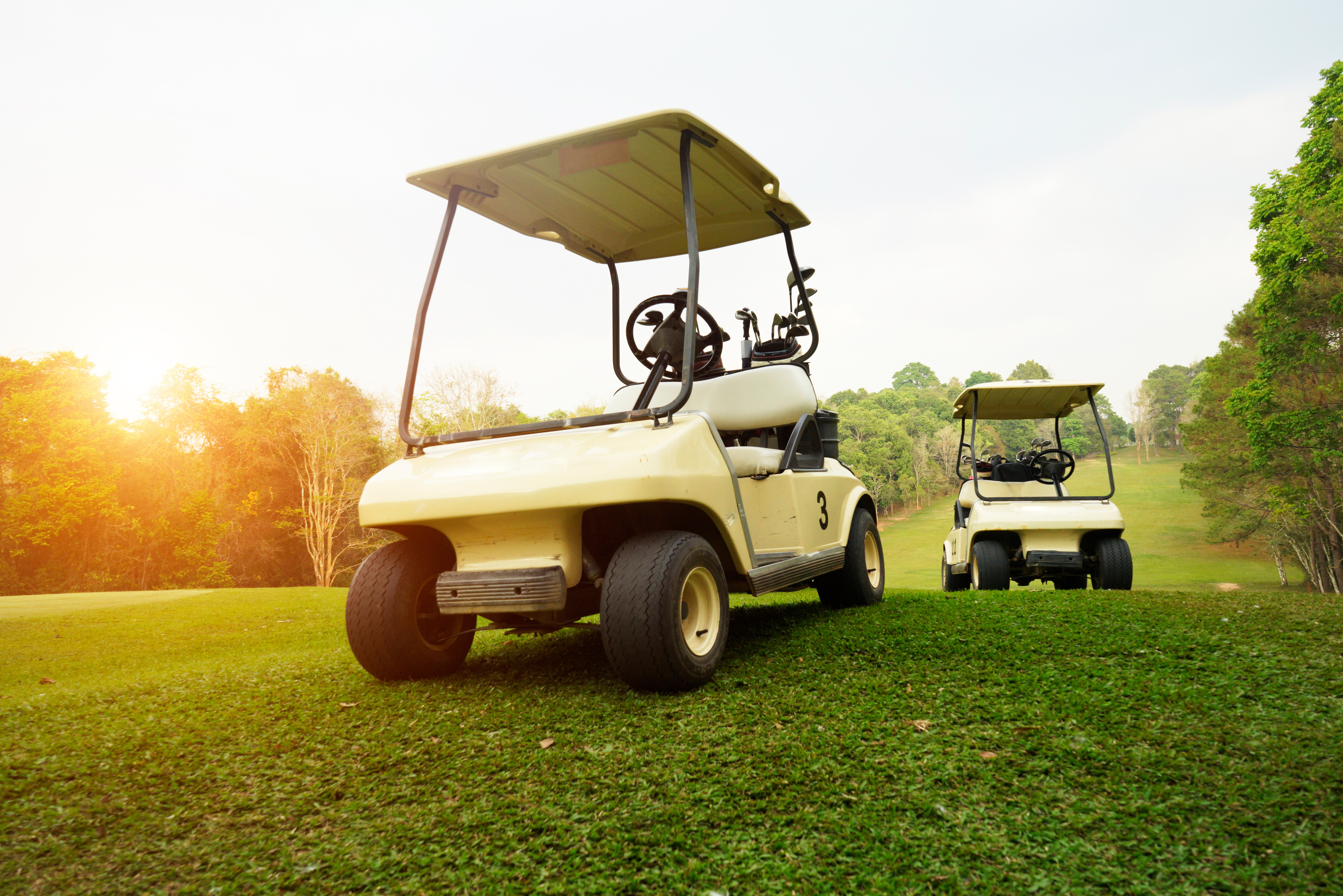 Two golf carts with sunset in background.
