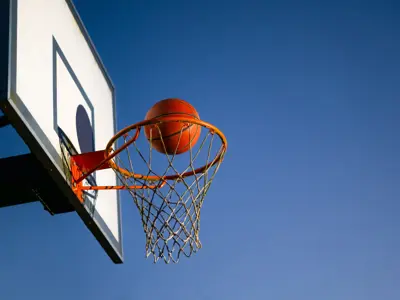 Basketball on the cusp of going into a basketball hoop.